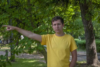 Sarı tişörtlü genç bir adam parmağını sağa doğru gösteriyor..