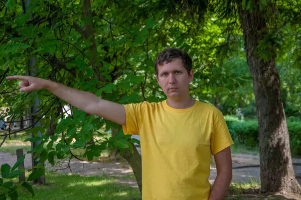 Sarı tişörtlü genç bir adam parmağını sağa doğru gösteriyor..