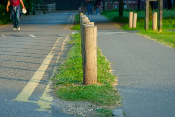 Solda bir çimen şeridi ve yolda boyalı sarı bir çizgi var. Sağda, bir yaya yolu paralel gidiyor. Yazıların ve gölgelerinin tekrarı kompozisyonda güçlü bir ritim ve perspektif hissi yaratır..
