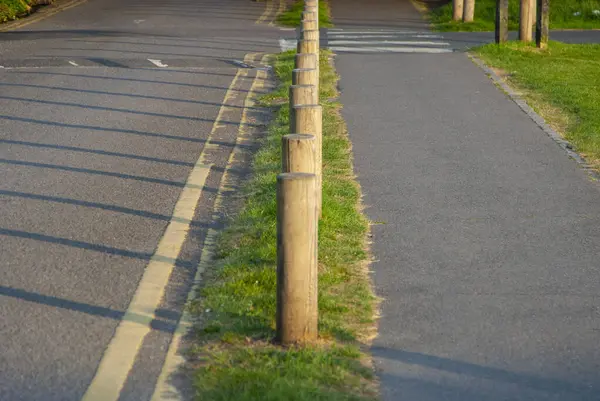 Bu fotoğraf, kısa tahta direklerle çevrili asfalt bir yolun görsel olarak çarpıcı bir görüntüsünü yakalıyor..