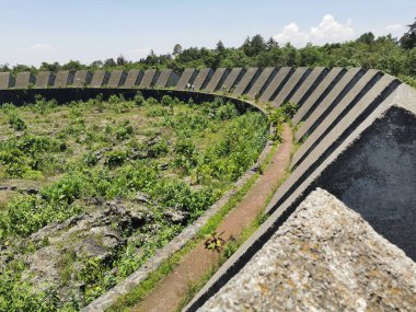 Geniş açılı ya da yüksek açılı bir çekim UNAM 'ın Espacio Escultorico' sunun geniş, dairesel beton yapısını ve segmentli, eğimli duvarlarını gözler önüne serer. Merkez bölge yemyeşil bitki örtüsüyle dolu ve dar bir toprak yol boyunca esiyor.