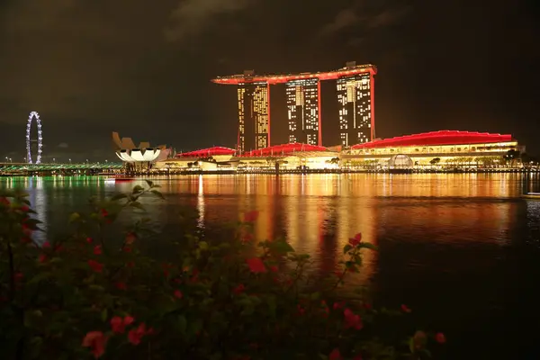 Marina Bay Sands 'e bakan Merlion Park' tan Singapur manzarası. Marina Körfezi 'nin ışıkları yüzeyinde çarpıcı yansımalar yaratırken tekneler yavaşça suda süzülüyor..