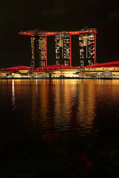 Marina Bay Sands 'e bakan Merlion Park' tan Singapur manzarası. Marina Körfezi 'nin ışıkları yüzeyinde çarpıcı yansımalar yaratırken tekneler yavaşça suda süzülüyor..