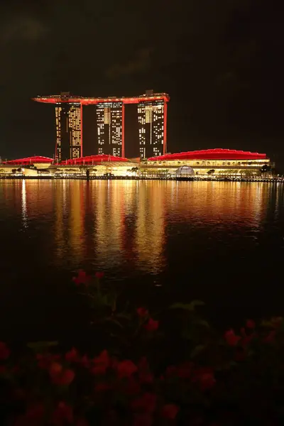 Marina Bay Sands 'e bakan Merlion Park' tan Singapur manzarası. Marina Körfezi 'nin ışıkları yüzeyinde çarpıcı yansımalar yaratırken tekneler yavaşça suda süzülüyor..