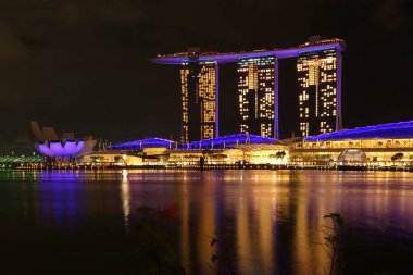 A stunning night view of Singapore from Merlion Park, with Marina Bay Sands in the background. Boats drift on the water as the radiant lights of Marina Bay cast beautiful reflections on its surface. clipart