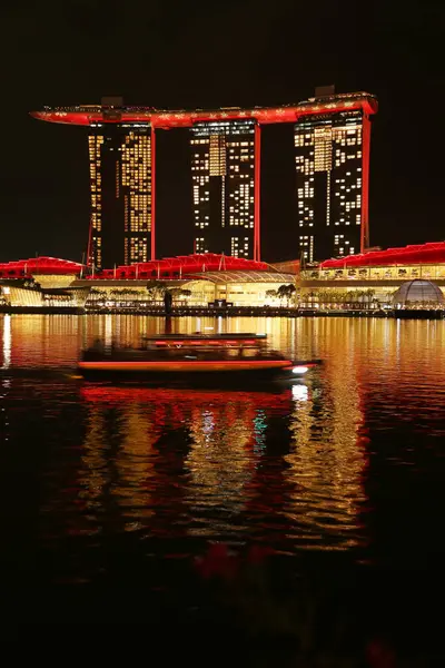 Marina Bay Sands 'e bakan Merlion Park' tan Singapur manzarası. Marina Körfezi 'nin ışıkları yüzeyinde çarpıcı yansımalar yaratırken tekneler yavaşça suda süzülüyor..
