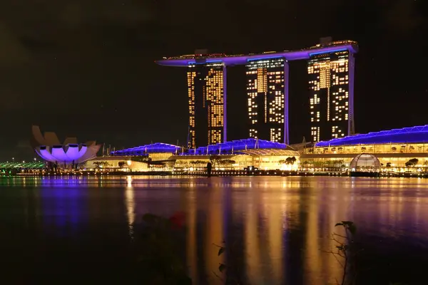 Singapur 'un Merlion Park' tan muhteşem bir gece görüntüsü. Arka planda Marina Bay Sands var. Marina Körfezi 'nin ışıl ışıl ışıkları yüzeyinde güzel yansımalar oluştururken tekneler denizde sürükleniyor..