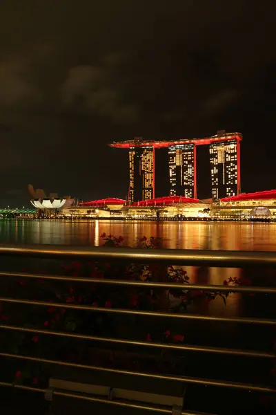 Singapur 'un Merlion Park' tan muhteşem bir gece görüntüsü. Arka planda Marina Bay Sands var. Marina Körfezi 'nin ışıl ışıl ışıkları yüzeyinde güzel yansımalar oluştururken tekneler denizde sürükleniyor..