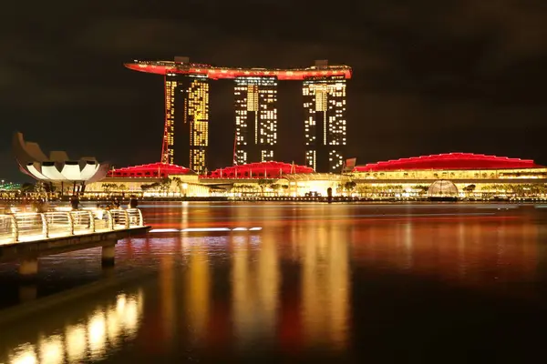 Singapur 'un Merlion Park' tan muhteşem bir gece görüntüsü. Arka planda Marina Bay Sands var. Marina Körfezi 'nin ışıl ışıl ışıkları yüzeyinde güzel yansımalar oluştururken tekneler denizde sürükleniyor..