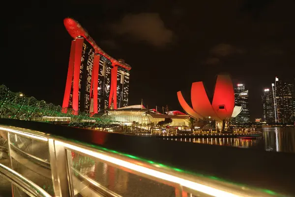 Marina Bay Sands 'e bakan Merlion Park' tan Singapur 'un gece görüşü. Marina Körfezi 'nin ışıkları yüzeyinde çarpıcı yansımalar yaratırken tekneler yavaşça suda süzülüyor..