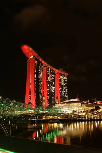 Marina Bay Sands 'e bakan Merlion Park' tan Singapur 'un gece görüşü. Marina Körfezi 'nin ışıkları yüzeyinde çarpıcı yansımalar yaratırken tekneler yavaşça suda süzülüyor..