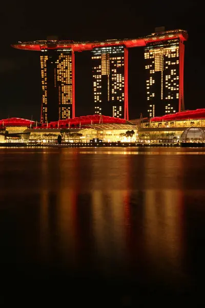 Marina Bay Sands 'e bakan Merlion Park' tan Singapur 'un gece görüşü. Marina Körfezi 'nin ışıkları yüzeyinde çarpıcı yansımalar yaratırken tekneler yavaşça suda süzülüyor..