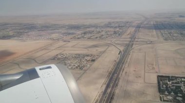 Geniş bir çöl şehrinin uçak penceresinden çekilmiş havadan görüntüsü. Şehir planlama, otoyollar ve sonsuz çöl manzaralarıyla çevrili yerleşim alanlarının altını çizmek.