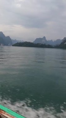 Kireçtaşı kayalıkları, sakin tropikal bir göldeki zümrüt yeşili sulardan dramatik bir şekilde yükselir. Arka planda puslu dağlar gizemli bir tılsım ekliyor. Huzurlu ve pitoresk bir cennet yaratıyor..