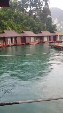 Bereketli tropikal ormanlar ve dramatik kireçtaşı uçurumları Tayland 'da Cheow Lan Gölü' nde yüzen ahşap villaları çevreler..