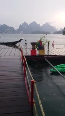 Bereketli, sisli bir dağ zemininde geleneksel ahşap teknelerle dolu sakin bir iskele. Sakin su ve yağmur huzurlu bir hava yaratır. Cheow Ian, Tayland.