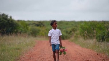 Young boy walking along dirt road with flowers in hand