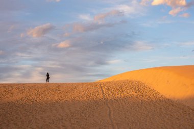Kum tepeciğinde duran bir kadın Bulutlar havada süzülüyor