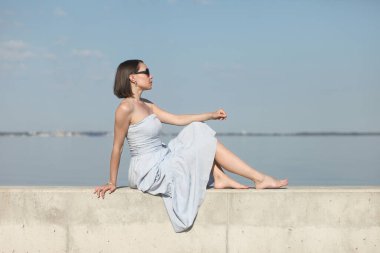 Deniz kenarındaki genç, narin kadın. Kıyafetler içinde poz veriyor.