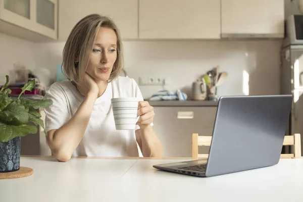 young woman in the kitchen with a mug and a laptop