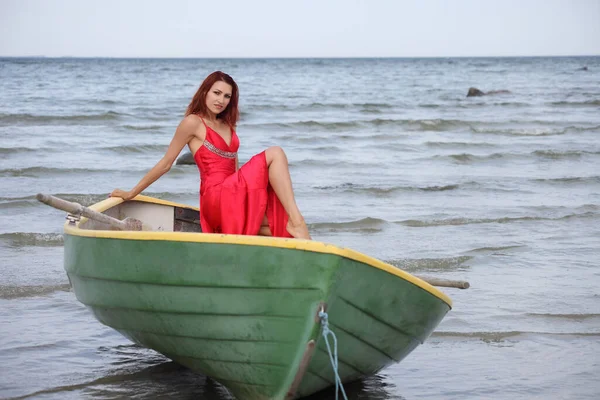 一个身材苗条的年轻女子 身穿红色连衣裙 海上有一条木船 — 图库照片
