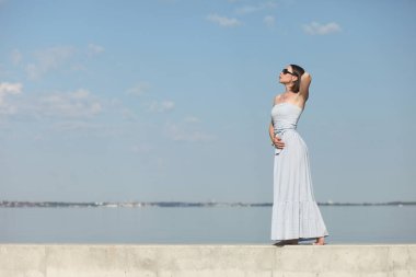 Deniz kenarındaki genç, narin kadın. Kıyafetler içinde poz veriyor.