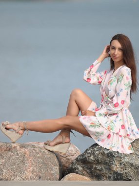 Deniz kenarındaki genç, narin kadın. Kıyafetler içinde poz veriyor.