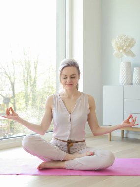 Genç ve güzel bir kadın büyük pencerenin yanında yoga yapıyor.