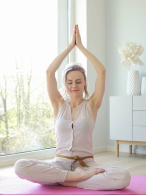 Genç ve güzel bir kadın büyük pencerenin yanında yoga yapıyor.