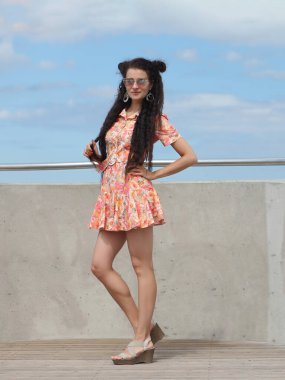 Deniz kenarındaki genç, narin kadın. Kıyafetler içinde poz veriyor.