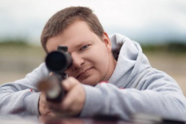 Bir adam tüfekten ateş etmek için optik görüş açısını hedefler.