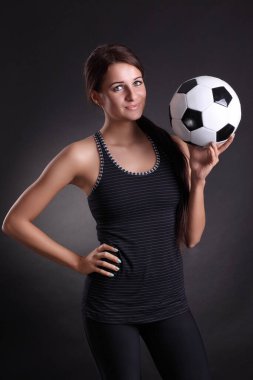 Siyah arka planda futbol topu olan genç bir kadın.