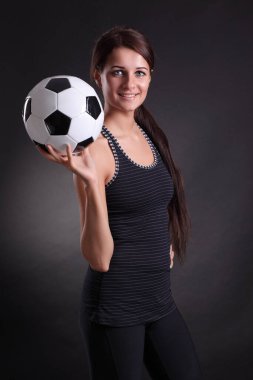 Siyah arka planda futbol topu olan genç bir kadın.