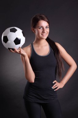 Siyah arka planda futbol topu olan genç bir kadın.