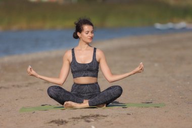Genç çıplak kadın vahşi bir plajda yoga yapıyor.
