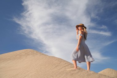 Genç bir kadın kumlu dağda elbise giymiş poz veriyor.
