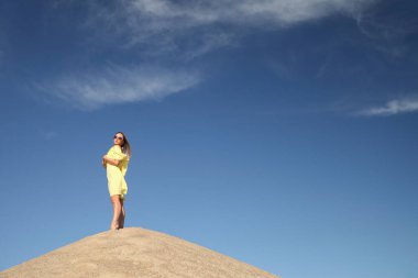 Genç bir kadın kumlu dağda elbise giymiş poz veriyor.