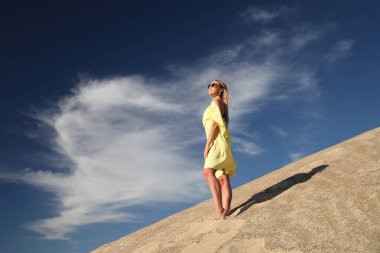 Genç bir kadın kumlu dağda elbise giymiş poz veriyor.