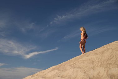 Genç bir kadın kumlu dağda elbise giymiş poz veriyor.