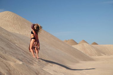 Genç bir kadın kumlu dağda elbise giymiş poz veriyor.