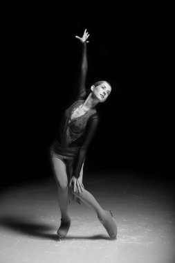 Genç bayan artistik patinajcı koyu arkaplanda poz veriyor