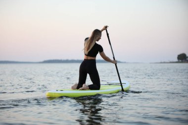 Suyun üzerinde elinde kürekle gezen genç bir kadın. Yaz, bir bitki özsuyunda yüzüyor..