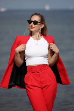 Deniz kenarındaki kırmızı takım elbiseli genç kadın.
