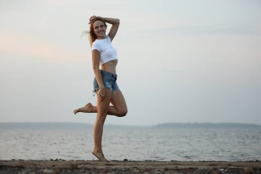 Mutlu kadın sahilde poz veriyor. Dantelli, kısa tişörtlü, kot şortlu, gülümseyen güzel bir sarışın.