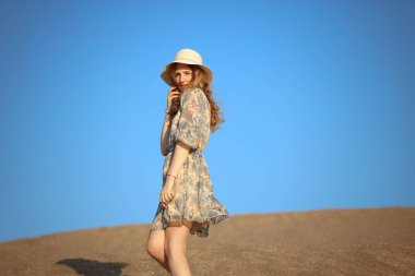 Genç bir kadın kumlu dağda elbise giymiş poz veriyor.