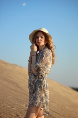 Genç bir kadın kumlu dağda elbise giymiş poz veriyor.