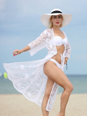 Kumsalda beyaz mayo giymiş genç bir kadın.