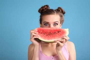 Mutlu genç bir kadın mavi arka planda taze karpuz diliminin tadını çıkarıyor.