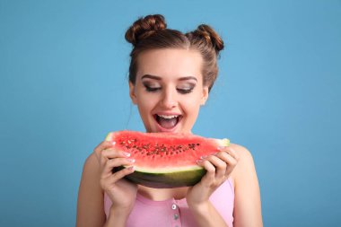 Mutlu genç bir kadın mavi arka planda taze karpuz diliminin tadını çıkarıyor.