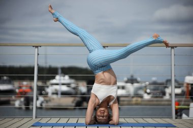 Teknelerin yanındaki tahta güvertede yoga yapan kadın.